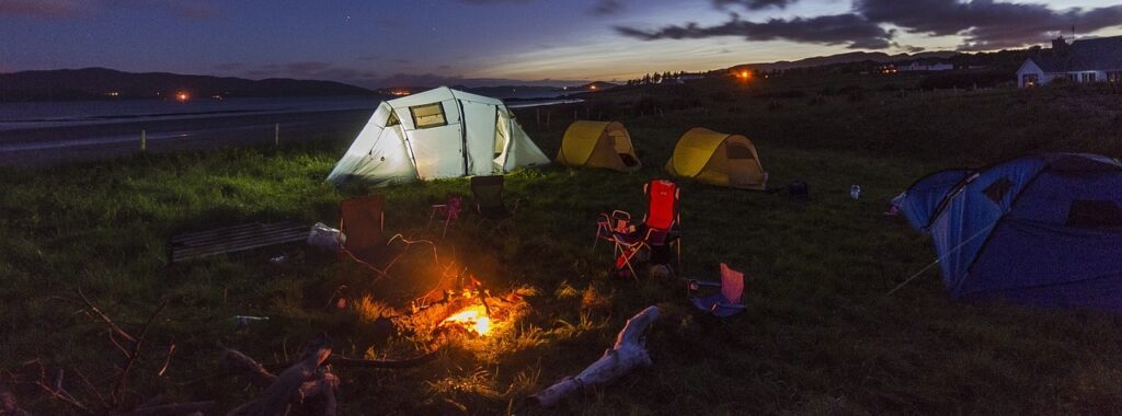 Group campsite at dusk with multiple tents and a glowing campfire on the coast